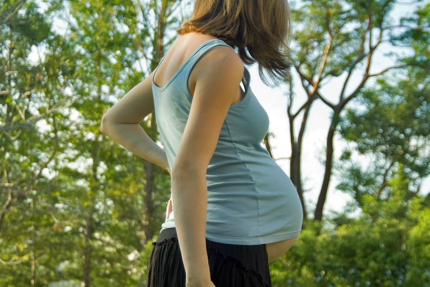A pregnant woman walking in a forest.