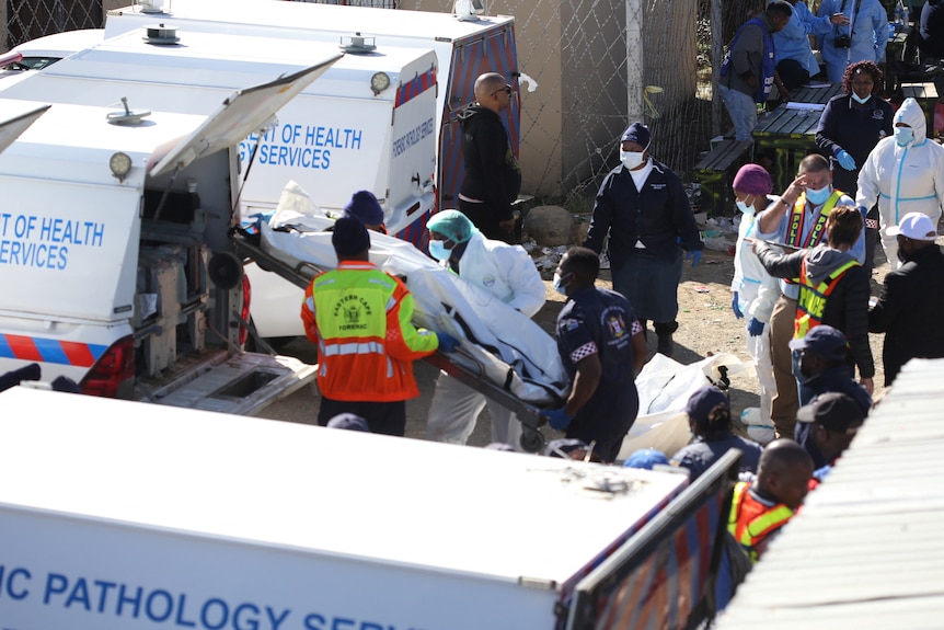 Forensic personnel load a covered body into a van.