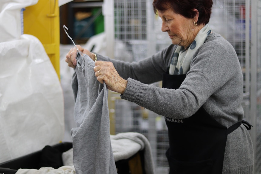 A woman wearing a gray jumper sorts through clothes at a second-hand shop.