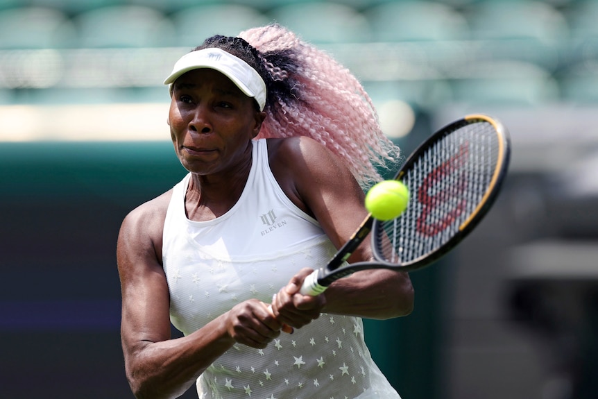 Venus Williams with teased pink hair grimaces as she hits a tennis ball.