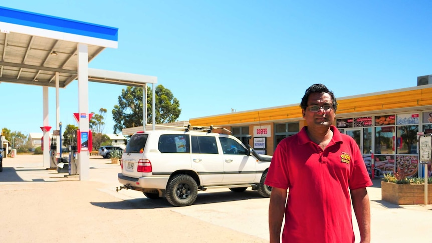 Indian man centre of frame at fuel roadhouse, background left  bowsers under canopy, right building