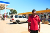 Indian man centre of frame at fuel roadhouse, background left  bowsers under canopy, right building
