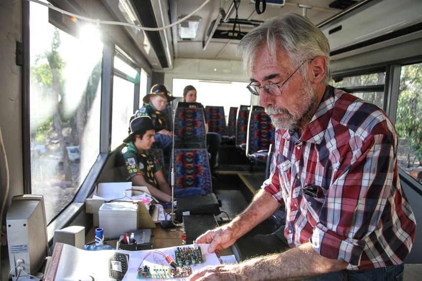 A man with a checkered shirt in a bus looks a radio equipment.