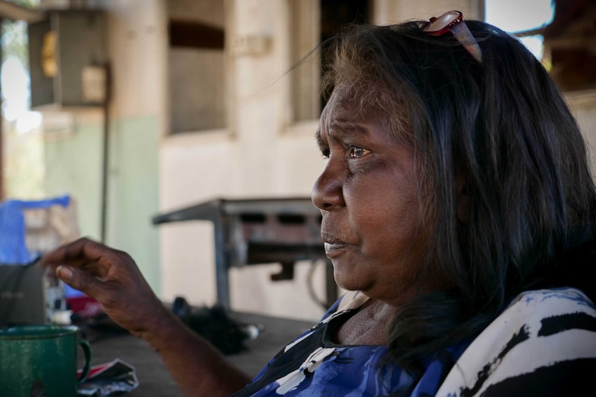 Woman sits at table in a shed with a cup of tea in the Kimberley.