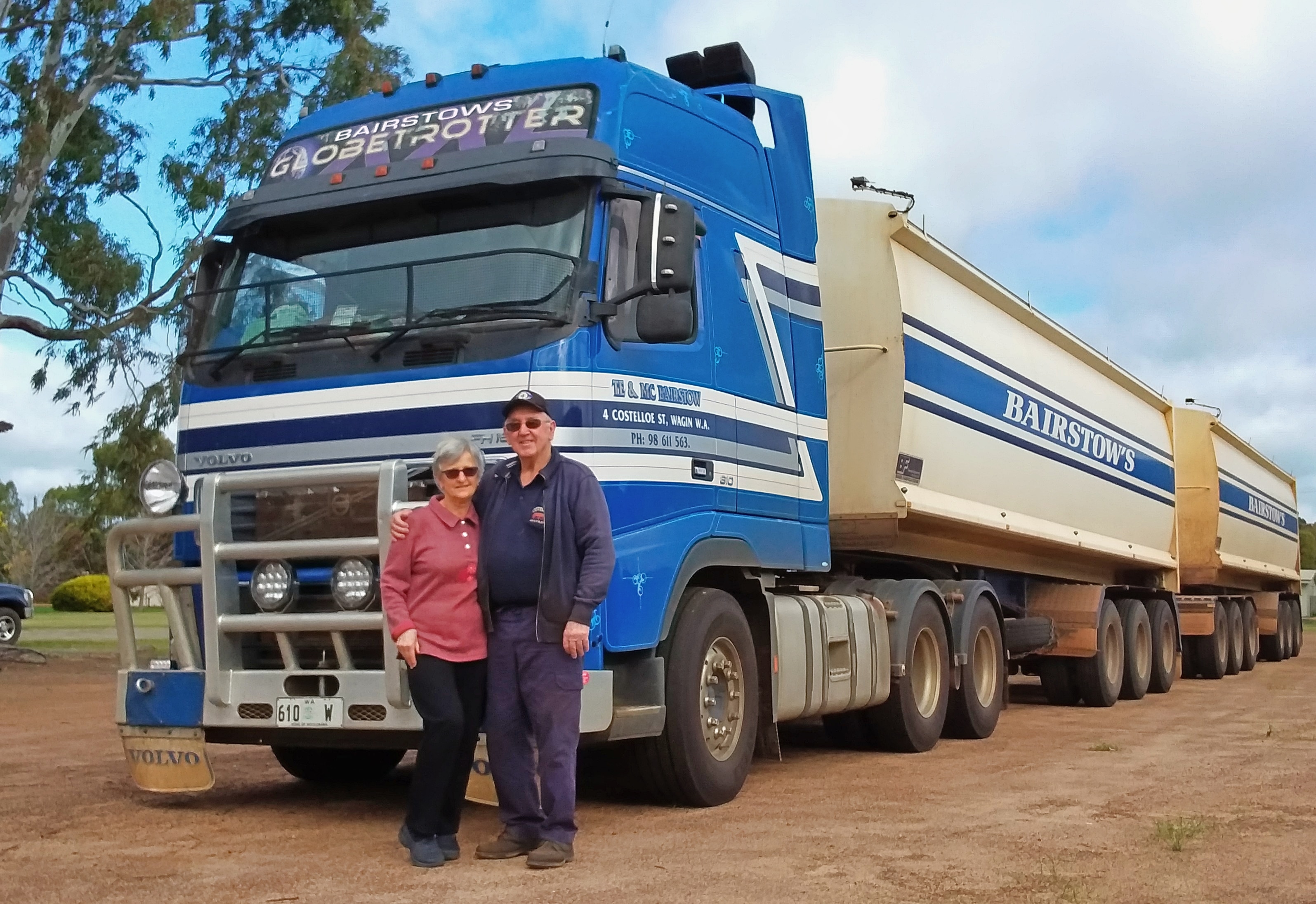Un hombre y una mujer se paran frente a un gran camión azul.