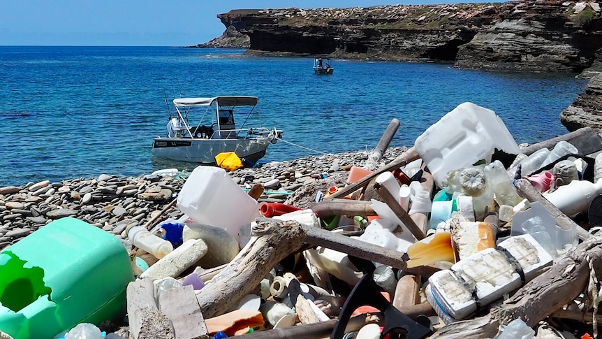 Various rubbish piled up on a rocky beach, looking over the water.