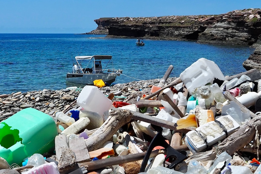 Various rubbish piled up on a rocky beach, looking over the water.