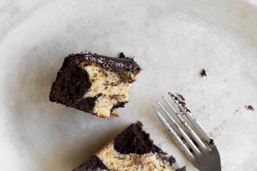 A slice of chocolate and vanilla marble cake with chocolate ganache topping, a classic and easy cake.