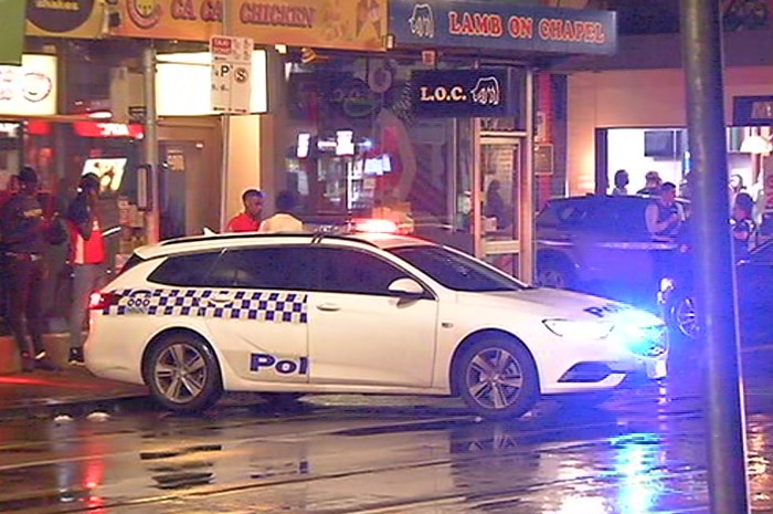 Police, a police car and members of the public stand on a wet street during dark early morning hours.
