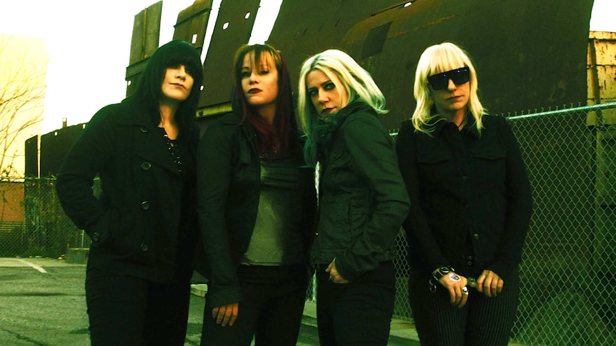 All women punk band L7 stand on the street in black clothes posing for the camera