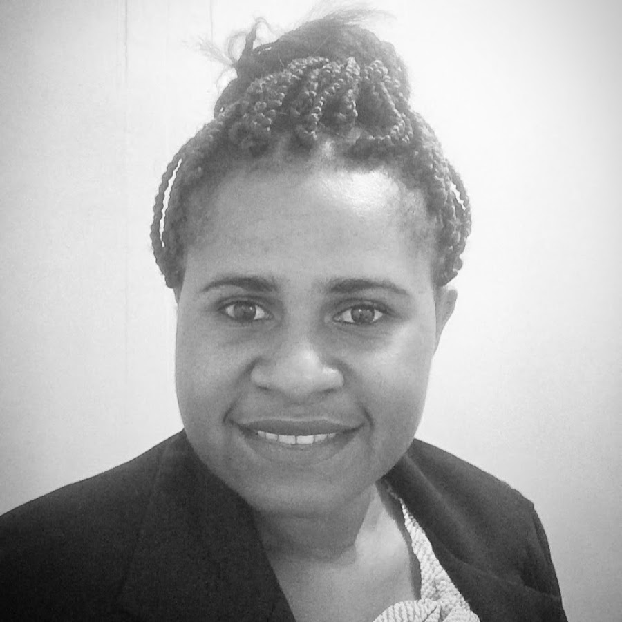 A greyscale photo of a Papua New Guinean woman with dark hair tied up in a bun smiling 