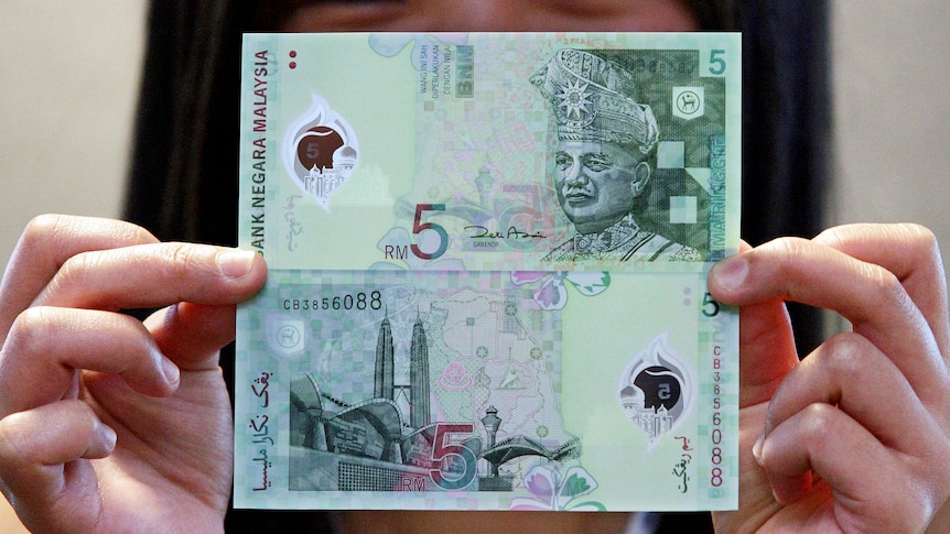 A Malaysian shows the front and back of the new five ringgit polymer notes.