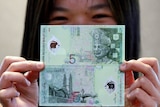 A Malaysian shows the front and back of the new five ringgit polymer notes.