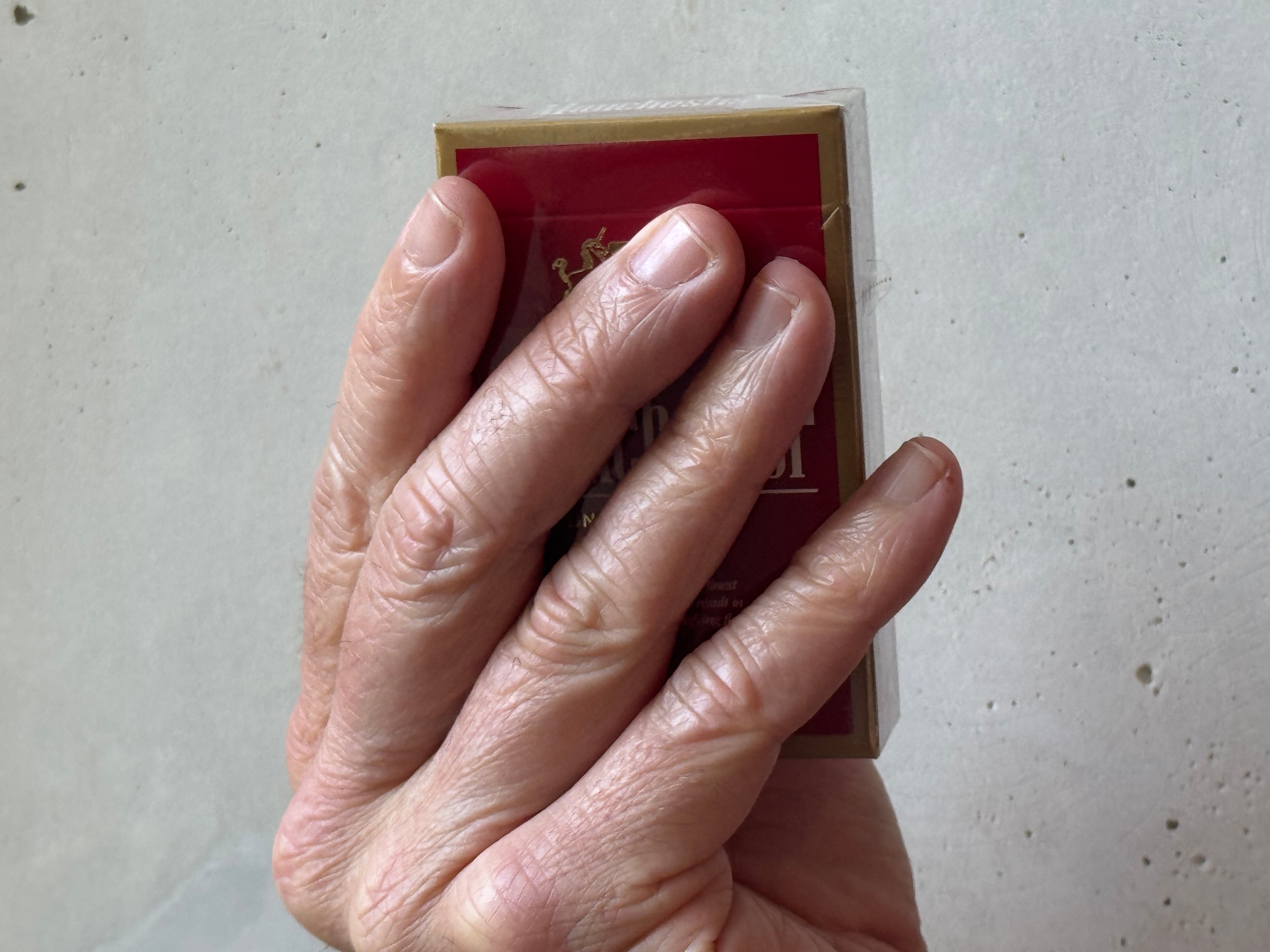 A hand holding a pack of Manchester Red cigarettes.