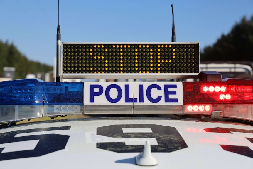 An illuminated "Stop" sign flashes on the top of a police car with flashing red and blue lights.