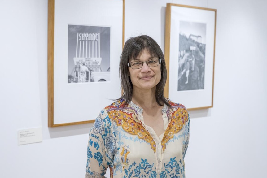 Colour photo of author Michelle Aung Thin standing in front of two artworks in gallery space.