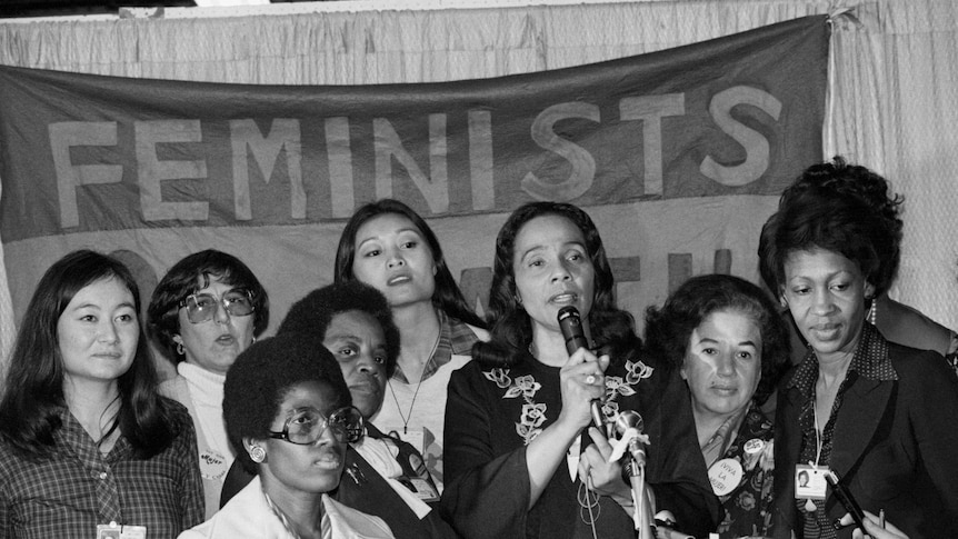 Coretta Scott King talks of the resolution on minority women's rights, standing supported by a group of other women.