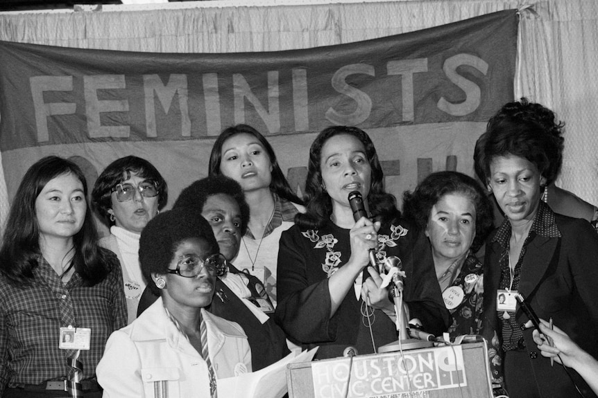 Coretta Scott King talks of the resolution on minority women's rights, standing supported by a group of other women.