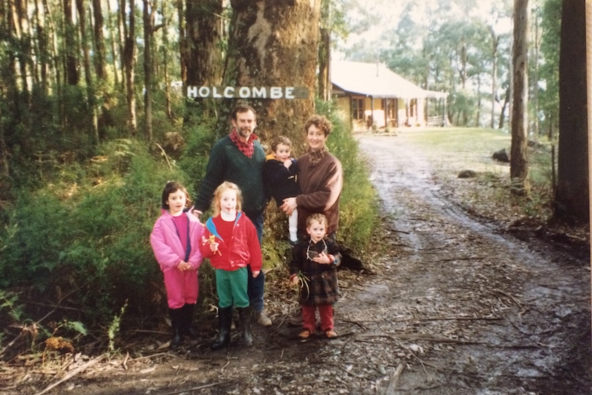 In an old family photograph, a young family stand by a bushy driveway next to a sign that reads HOLCOMBE.