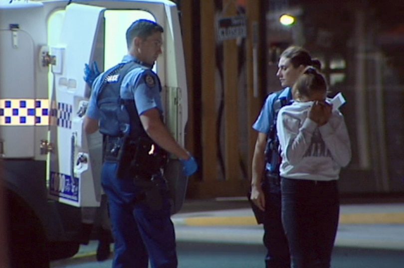 A woman appears upset as she hides her face in her jumper as she stands next to officers.