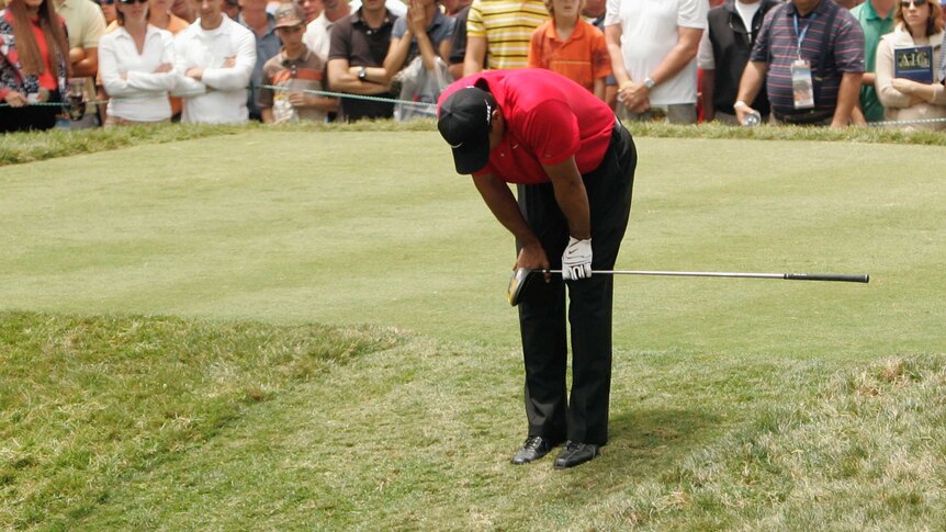 A golfer bends over on the tee in obvious discomfort holding his knee.