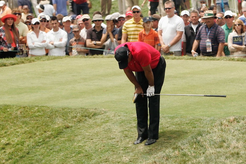 A golfer bends over on the tee in obvious discomfort holding his knee.