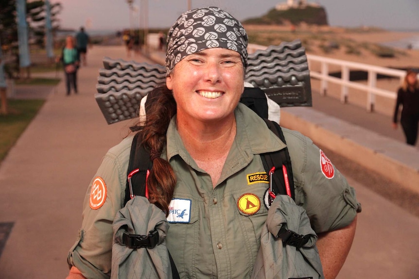 Smiling woman wearing hiking gear pictured at sunset near a lighthouse.