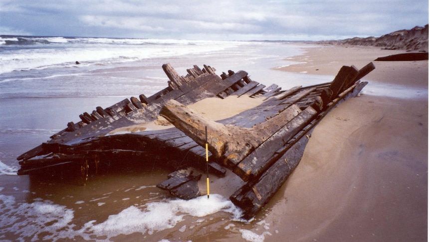 A wooden hull of a shipwreck lies on a beach. 