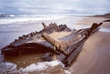 A wooden hull of a shipwreck lies on a beach. 
