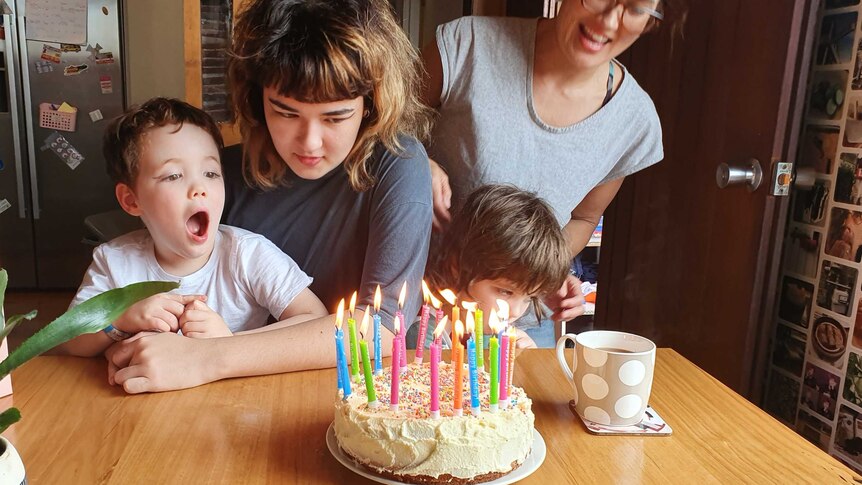 Two women and two children behind a table with a birthday cake on it.