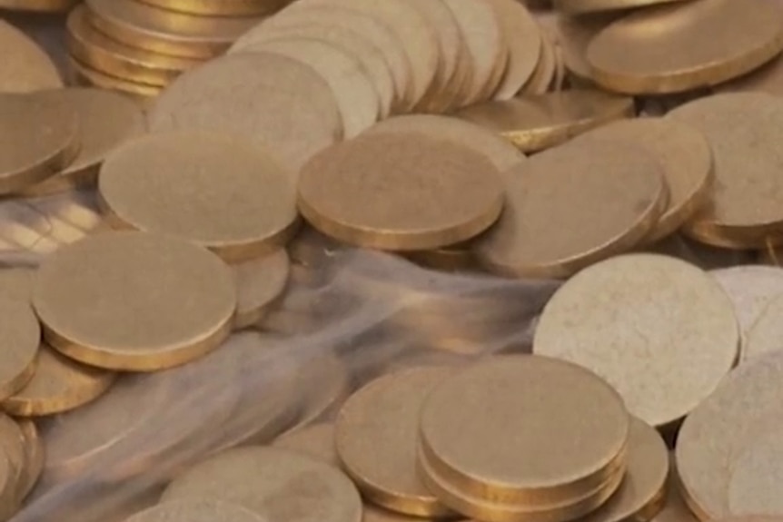 A pile of gold-coloured coins  sits on a light-coloured backdrop