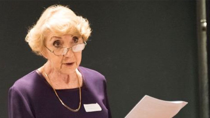 A woman wearing glasses addressing a room with microphone and podium beside her