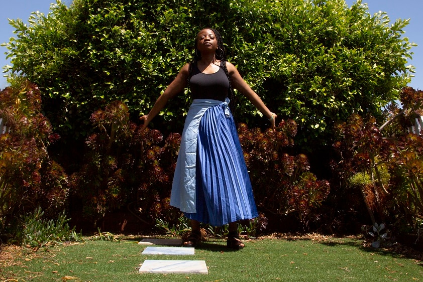 A young girl in a blue skirt raises her arms in the sunlight
