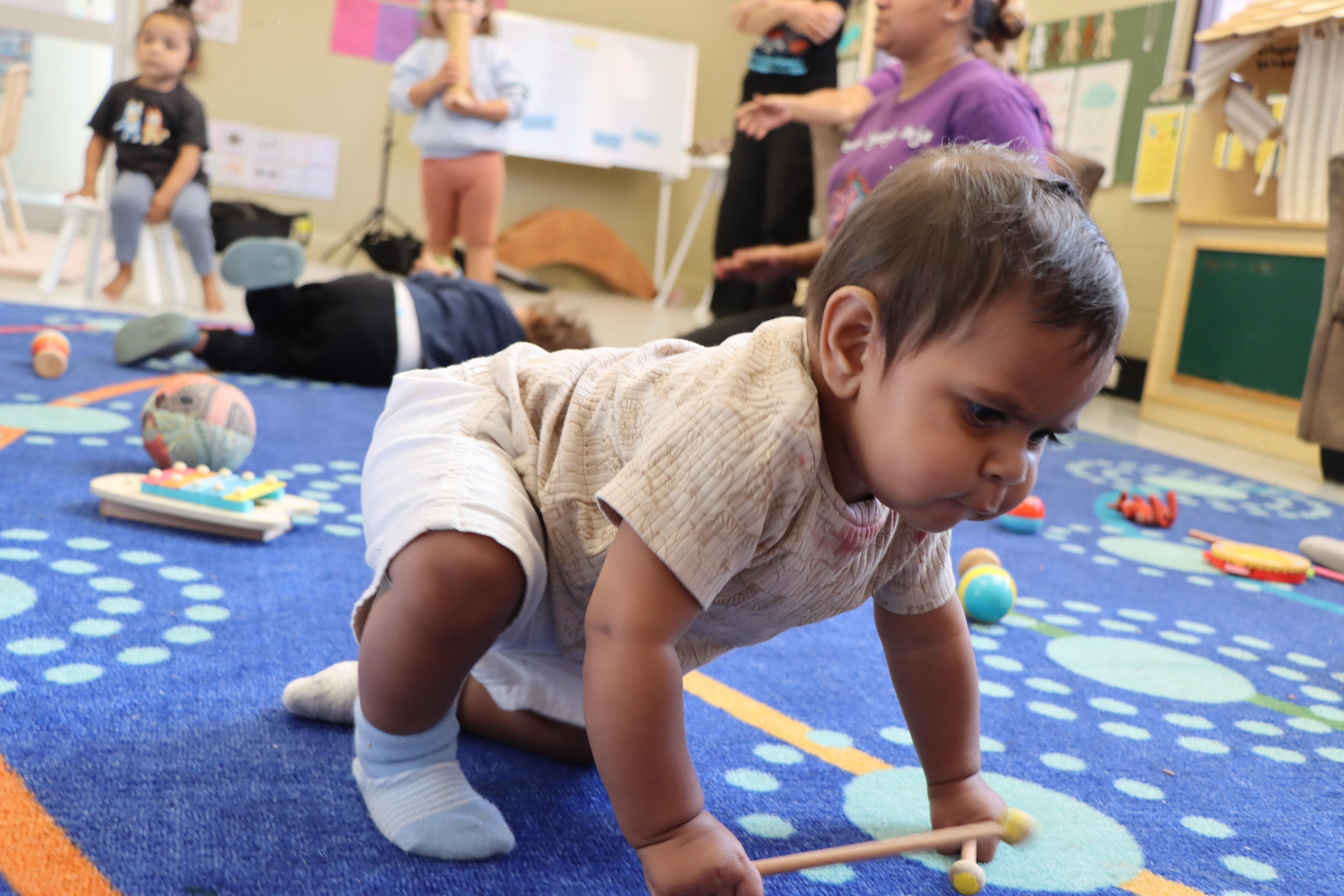 A baby plays on a colourful carpet.