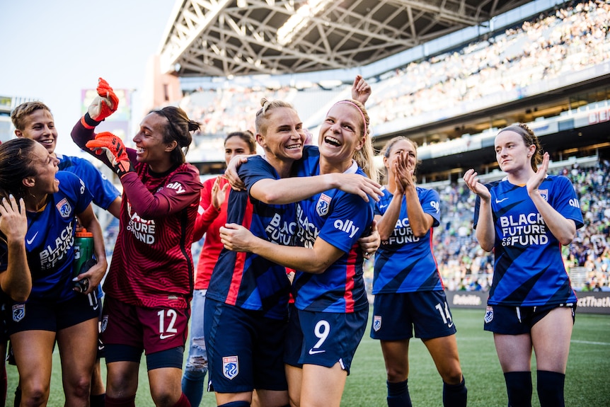 Jess Fishlock hugs a teammate inside a stadium as other teammates clap around her