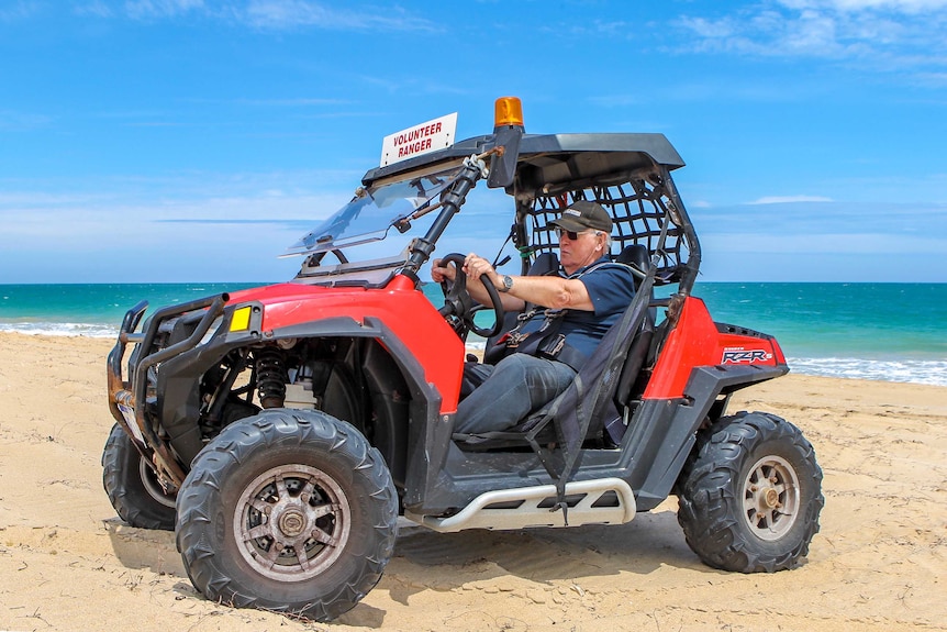 An elderly man sits in a red ATV on a beach