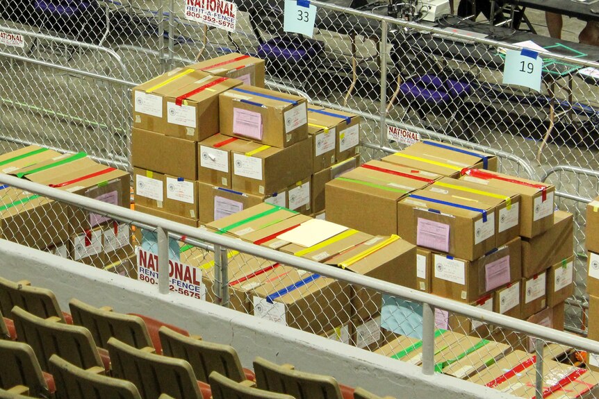 cardboard boxes with colorful tape sit behind a chain-link fence 