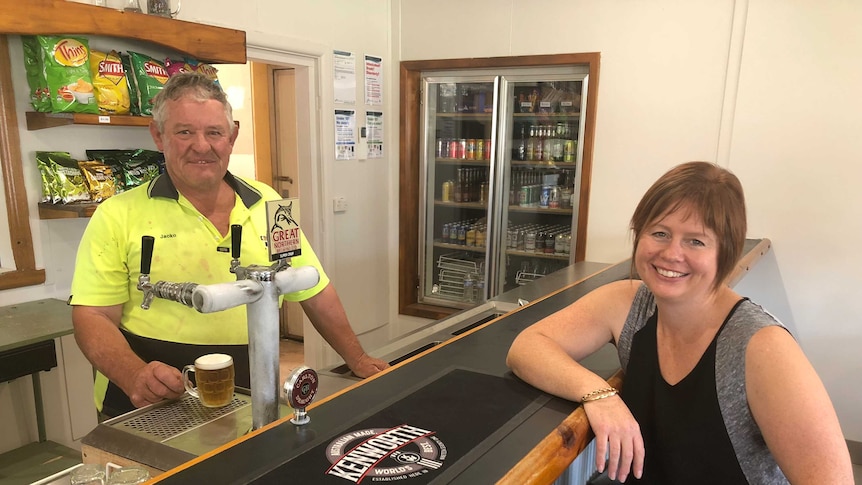 a man standing behind a bar holding a beer a woman sitting on other side of the bar smiling
