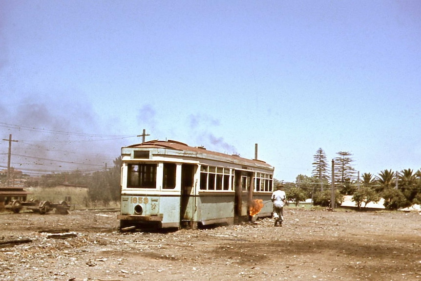 A man walks toward an old tram with a flame