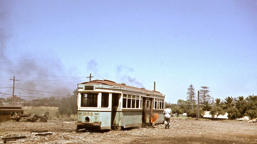 A man walks toward an old tram with a flame