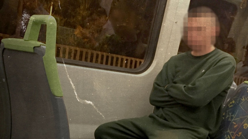 A man in a green prison tracksuit sits in a train with arms folded.