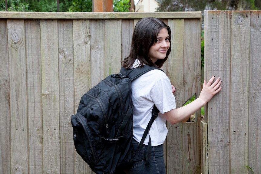 A young girl in a backpack opens her gate to go to school