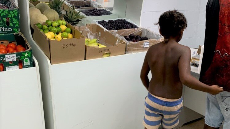 An Aboriginal boy standing in front of a fruit stand