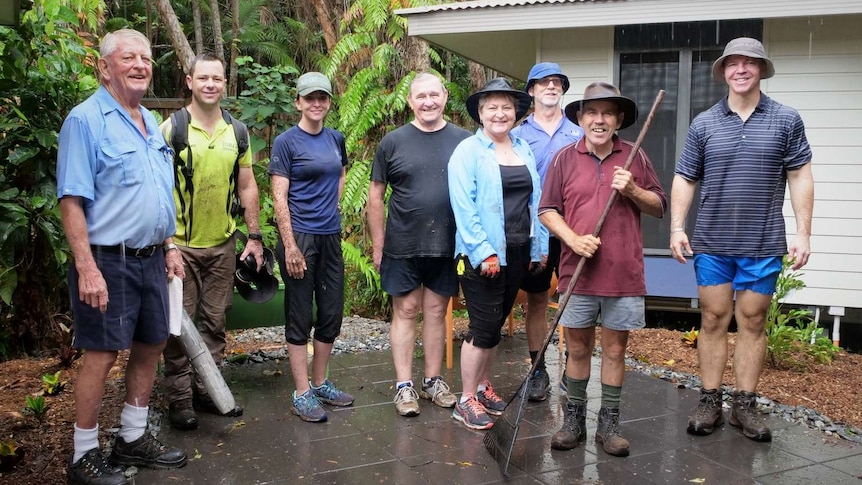 Group of people standing outside in the rain with one holding a rake