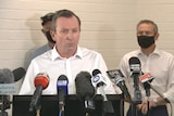 A man in a white shirt stands behind a bank of microphones.