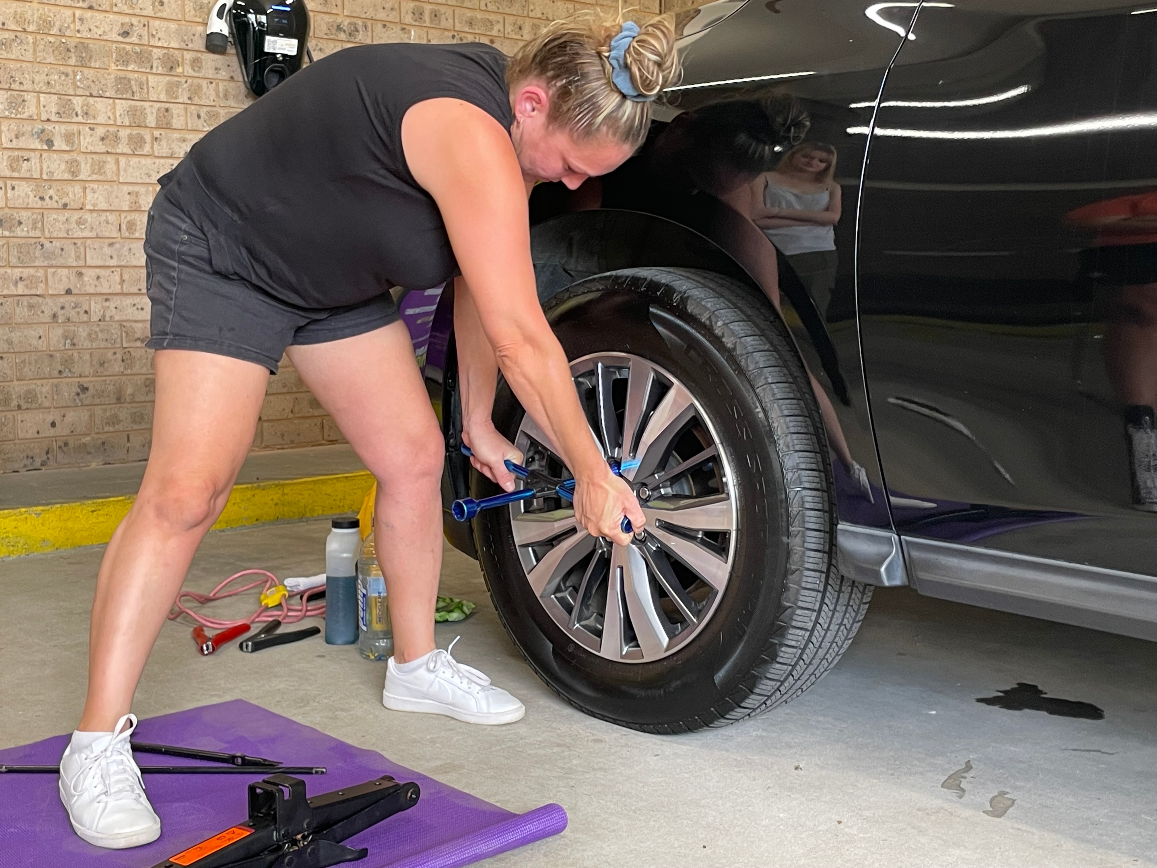 A woman in shorts holds a wrench to a tyre.