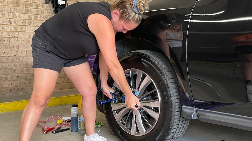 A woman in shorts holds a wrench to a tyre.