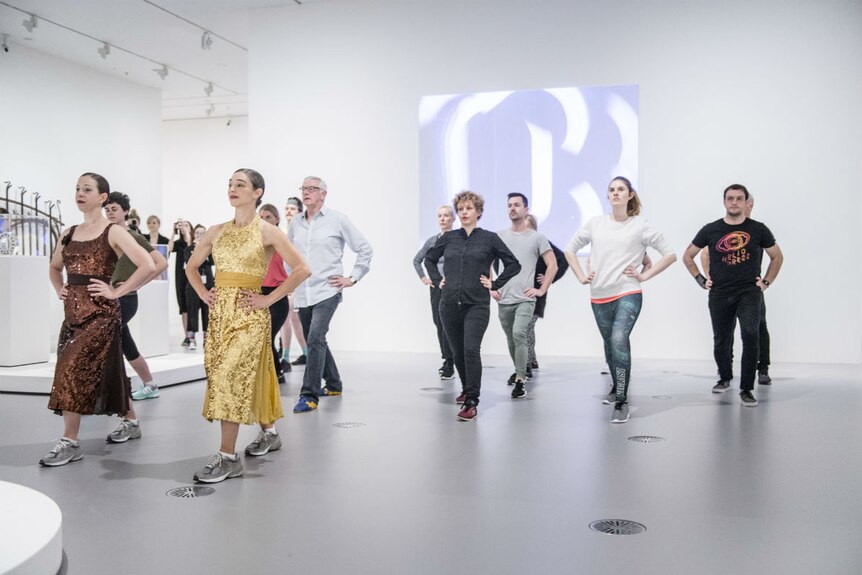 People do lunges in a white room inside a gallery.