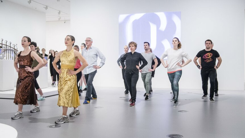 People do lunges in a white room inside a gallery.