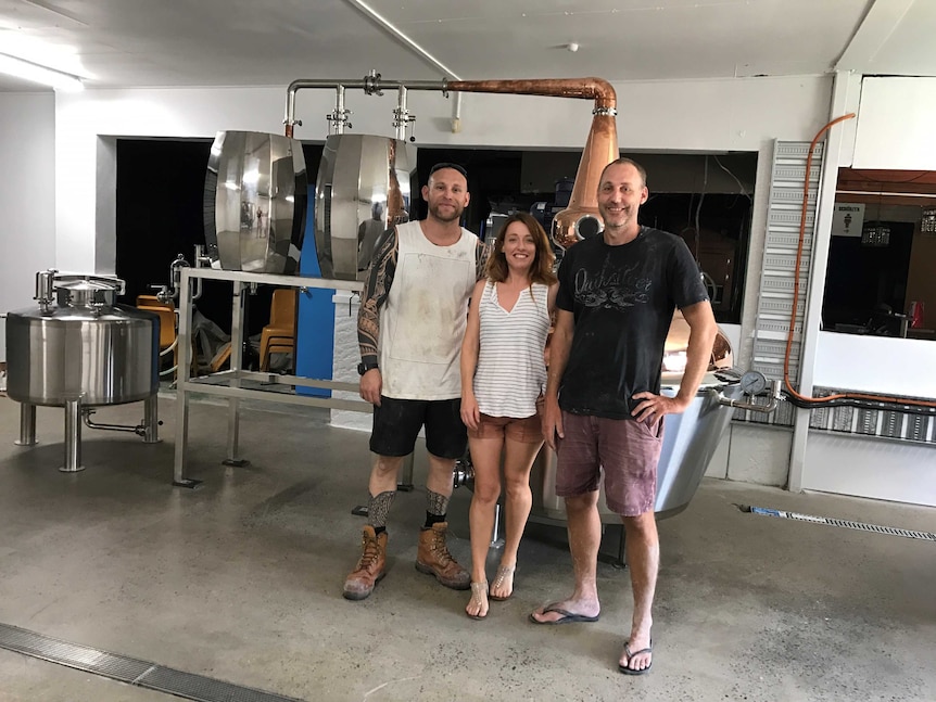 Three people stand next a distilling kit